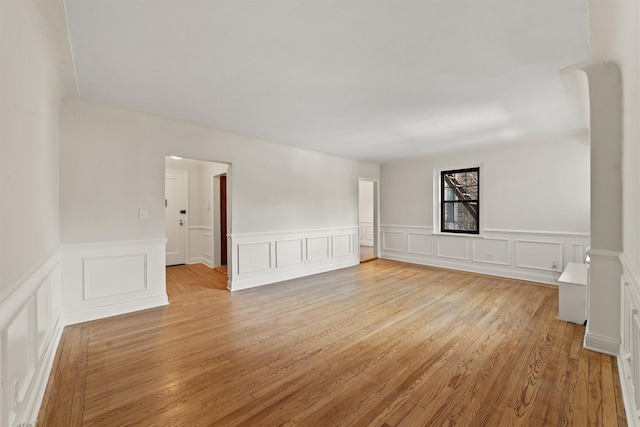 spare room featuring a decorative wall, wainscoting, and light wood-type flooring