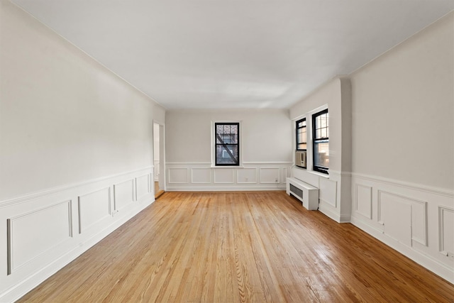 unfurnished room featuring light wood-style floors, a wainscoted wall, and a decorative wall