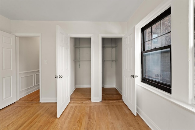 unfurnished bedroom with multiple closets, light wood-style flooring, and baseboards
