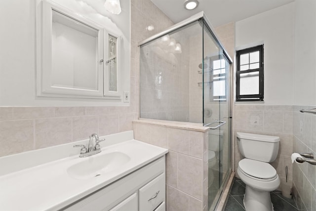 bathroom with tile walls, a stall shower, toilet, vanity, and tile patterned flooring