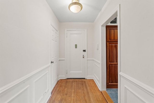 doorway featuring light wood-type flooring, a decorative wall, and a wainscoted wall