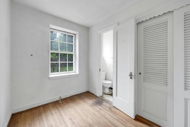 unfurnished bedroom with light wood-style floors, baseboards, a closet, and connected bathroom