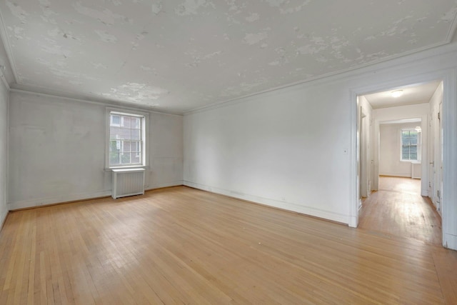 spare room featuring radiator, light wood-style flooring, baseboards, and crown molding