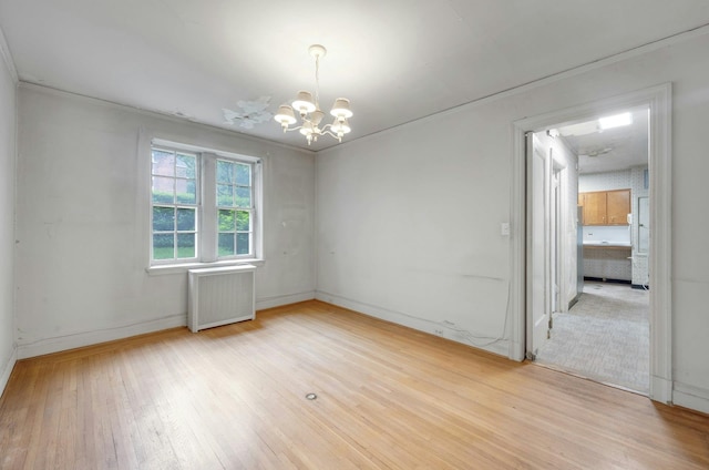 spare room featuring radiator, a chandelier, light wood finished floors, baseboards, and ornamental molding