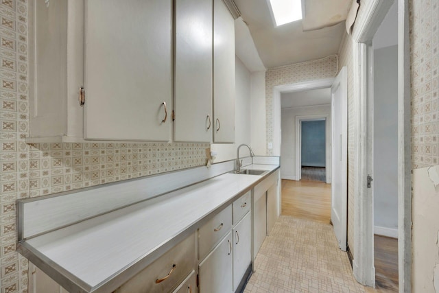 kitchen featuring a sink, wallpapered walls, light countertops, tasteful backsplash, and light tile patterned flooring