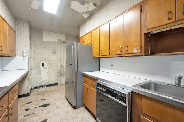 kitchen featuring black dishwasher, wallpapered walls, freestanding refrigerator, brown cabinetry, and a sink