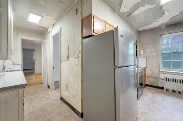 kitchen featuring radiator, freestanding refrigerator, wallpapered walls, a sink, and light countertops