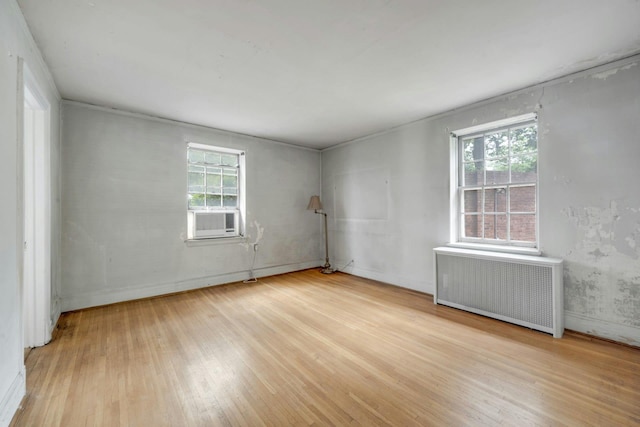 empty room featuring radiator heating unit, wood finished floors, plenty of natural light, and cooling unit