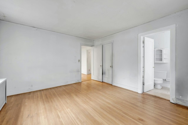 unfurnished bedroom featuring light wood-type flooring, ensuite bath, and baseboards