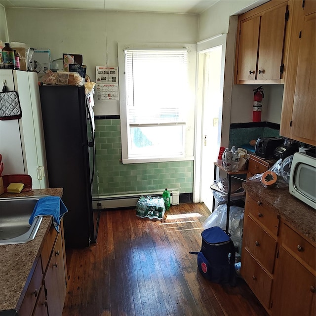 27 Coolidge Ave, Amityville, NY 11701 - kitchen featuring freestanding refrigerator, dark wood-type flooring, brown cabinets, a baseboard heating unit, and dark countertops