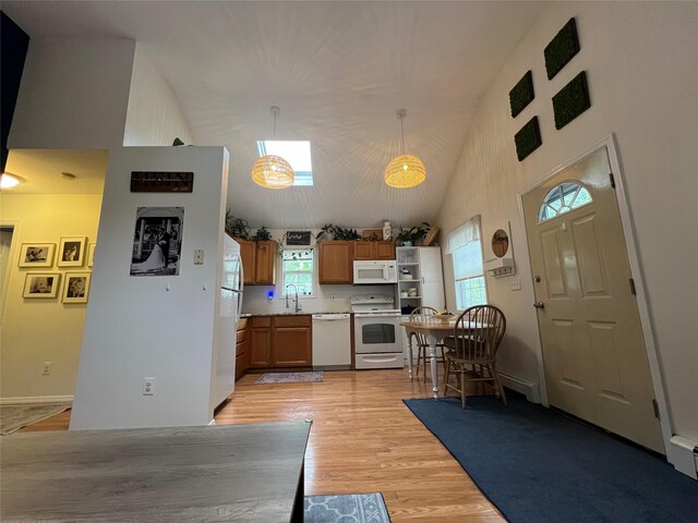 kitchen featuring white appliances, a sink, light wood finished floors, brown cabinets, and light countertops
