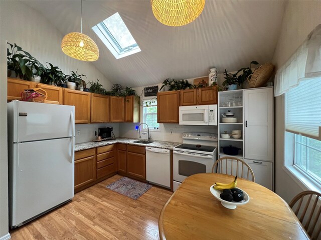 kitchen with white appliances, vaulted ceiling, light wood-style floors, a skylight, and a sink