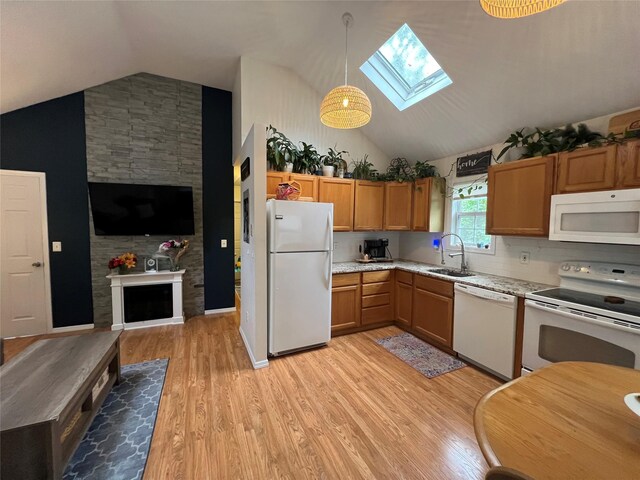 kitchen featuring white appliances, lofted ceiling, a sink, a fireplace, and a skylight