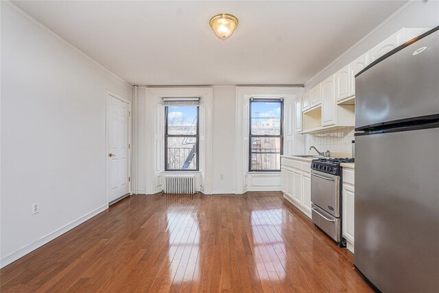 146 Nelson St, Brooklyn, NY 11231 - kitchen with appliances with stainless steel finishes, radiator, hardwood / wood-style floors, white cabinets, and backsplash