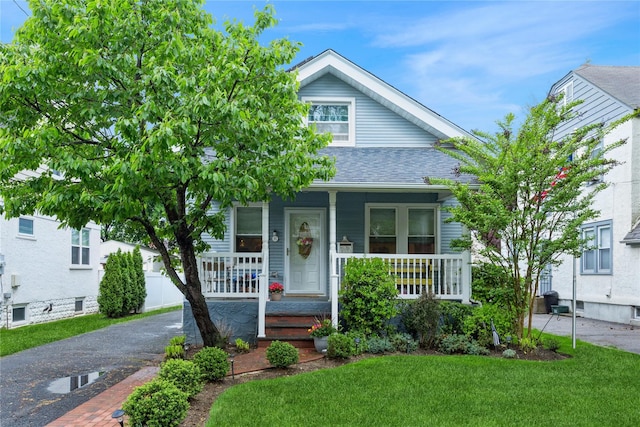 view of front of home featuring covered porch, a front lawn, and roof with shingles