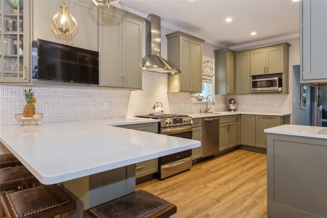 kitchen with appliances with stainless steel finishes, wall chimney exhaust hood, crown molding, light wood finished floors, and a breakfast bar