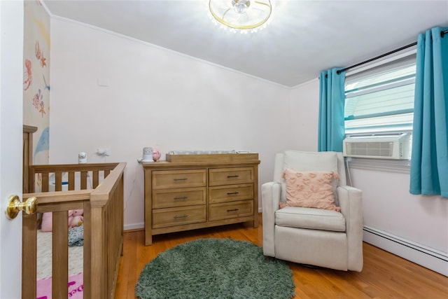 bedroom featuring a baseboard heating unit, light wood-style floors, ornamental molding, and a crib