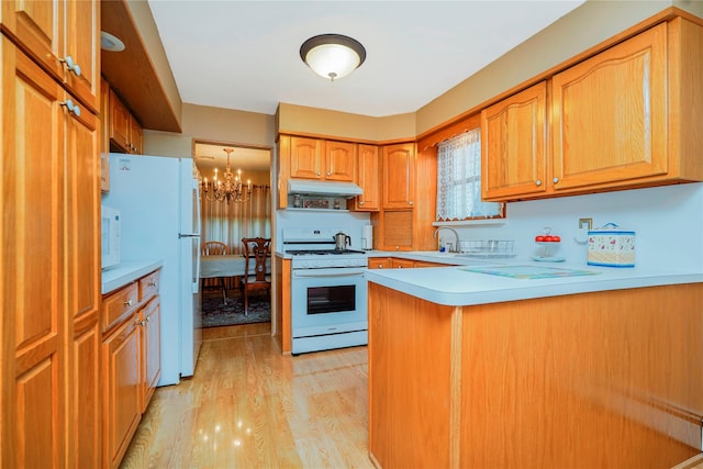 kitchen featuring white appliances, under cabinet range hood, a chandelier, a peninsula, and light countertops
