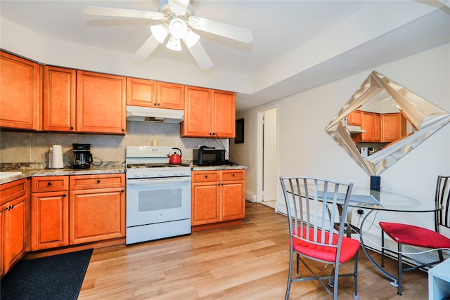 kitchen featuring white range with gas cooktop, under cabinet range hood, light wood-style flooring, and decorative backsplash