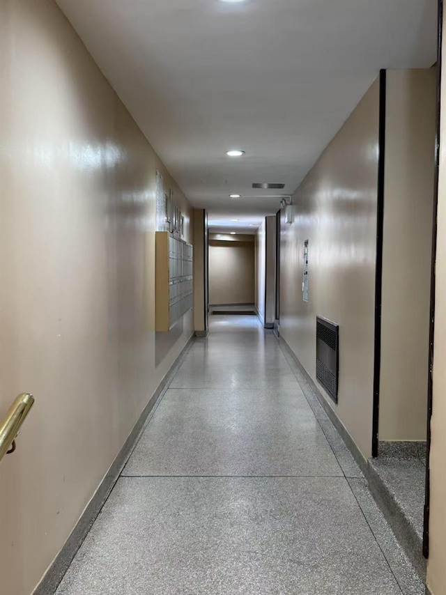 hall featuring speckled floor, baseboards, and heating unit