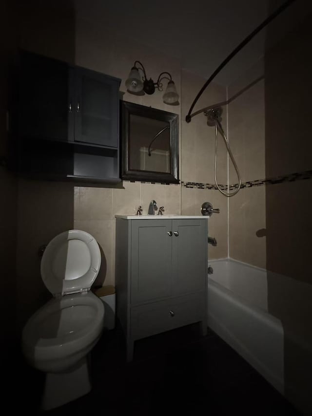 bathroom with tile walls, washtub / shower combination, vanity, and toilet