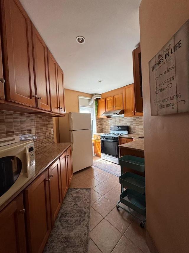 kitchen with white appliances, decorative backsplash, light tile patterned floors, under cabinet range hood, and brown cabinetry