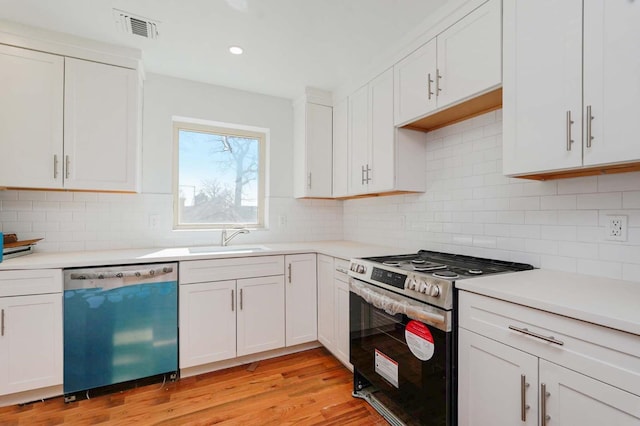 kitchen featuring dishwasher, gas stove, a sink, light countertops, and white cabinetry