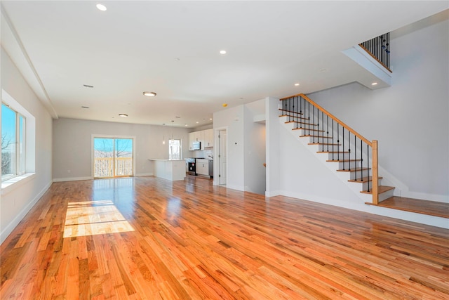unfurnished living room with stairway, light wood-style flooring, recessed lighting, and baseboards