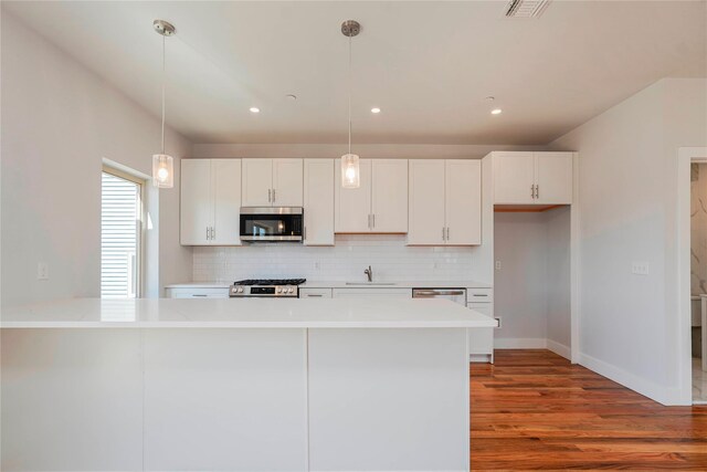 kitchen with stainless steel microwave, wood finished floors, tasteful backsplash, white cabinetry, and recessed lighting