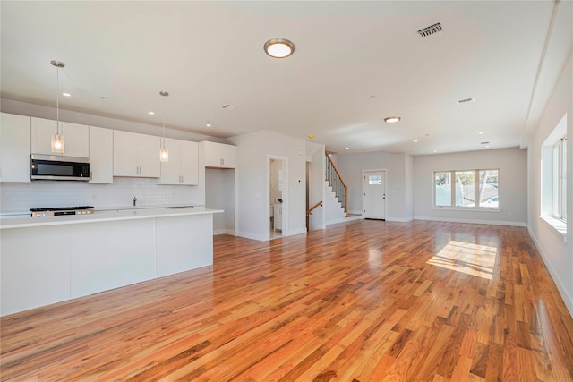 kitchen with stainless steel microwave, recessed lighting, white cabinets, tasteful backsplash, and light wood-style flooring