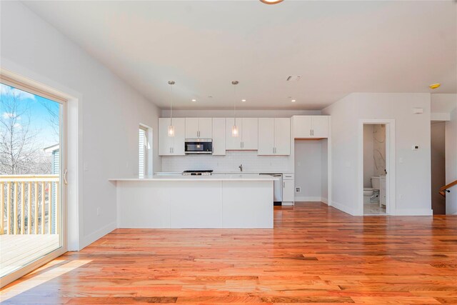 kitchen featuring stainless steel appliances, a peninsula, light wood-type flooring, white cabinets, and backsplash