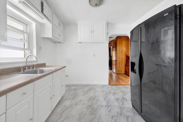 1230 Arnow Ave, Bronx, NY 10469 - kitchen featuring black fridge with ice dispenser, a sink, white cabinetry, light countertops, and arched walkways