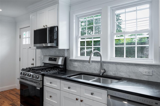 381 Wading River Rd, Manorville, NY 11949 - kitchen featuring appliances with stainless steel finishes, a sink, dark countertops, white cabinets, and ornamental molding