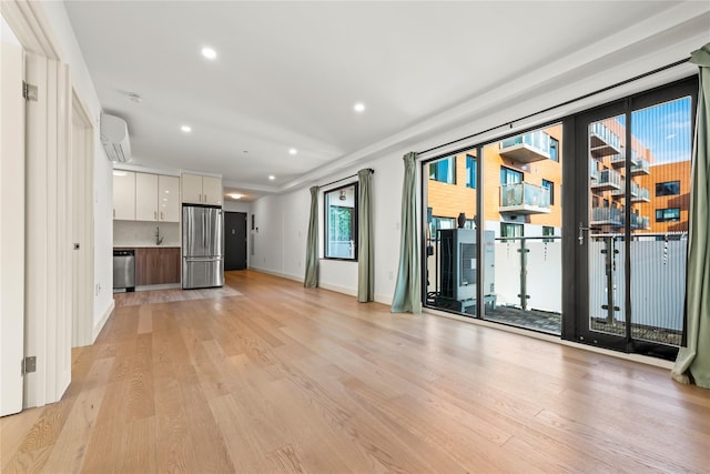 unfurnished living room with light wood finished floors, healthy amount of natural light, an AC wall unit, recessed lighting, and baseboards