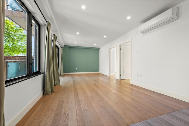 spare room featuring a wall mounted air conditioner, light wood-style flooring, recessed lighting, and baseboards
