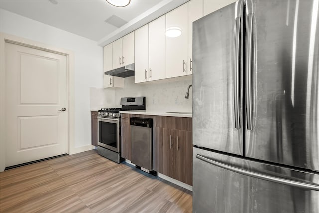 kitchen with appliances with stainless steel finishes, under cabinet range hood, a sink, light countertops, and white cabinetry