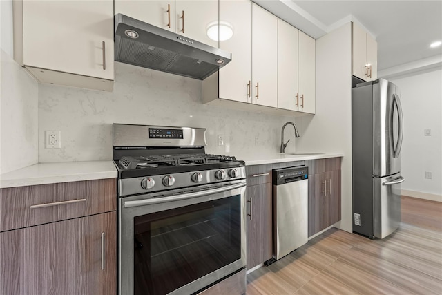 kitchen featuring appliances with stainless steel finishes, under cabinet range hood, a sink, light countertops, and white cabinets
