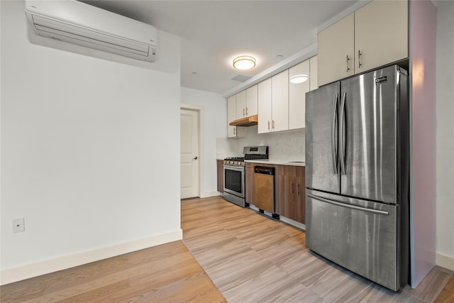 kitchen featuring appliances with stainless steel finishes, a wall unit AC, under cabinet range hood, light countertops, and light wood-type flooring