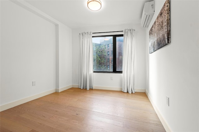 spare room featuring a wall mounted AC, light wood-type flooring, and baseboards