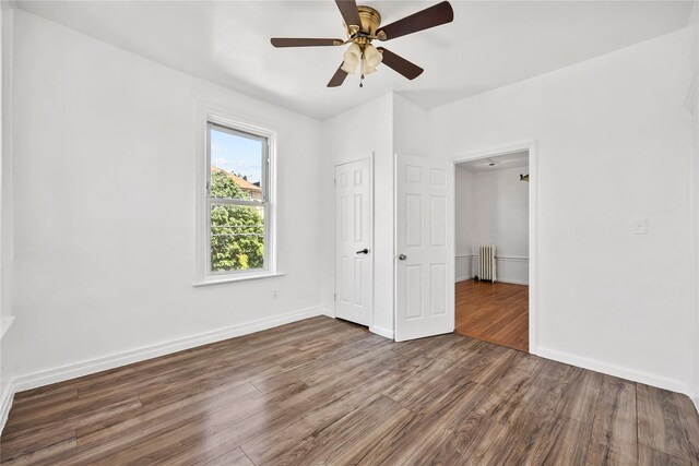 unfurnished bedroom featuring radiator heating unit, wood finished floors, baseboards, and a ceiling fan