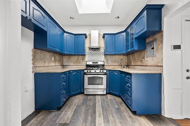 kitchen with stainless steel gas stove, wall chimney exhaust hood, blue cabinets, a skylight, and electric panel