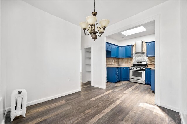 kitchen with blue cabinets, gas stove, wall chimney exhaust hood, a skylight, and tasteful backsplash