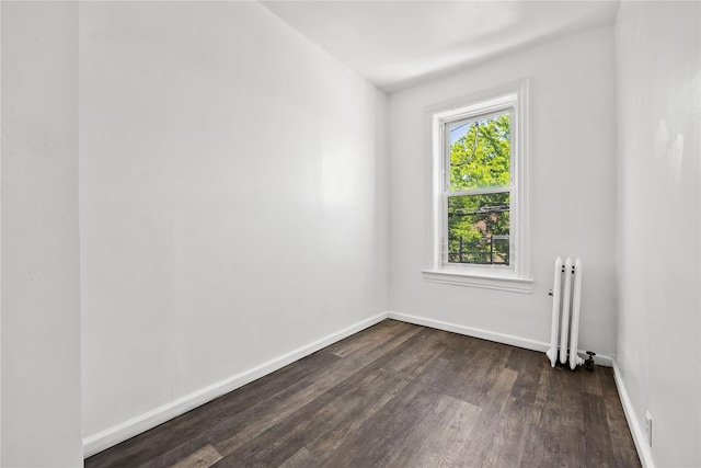 spare room featuring radiator heating unit, dark wood-style floors, and baseboards