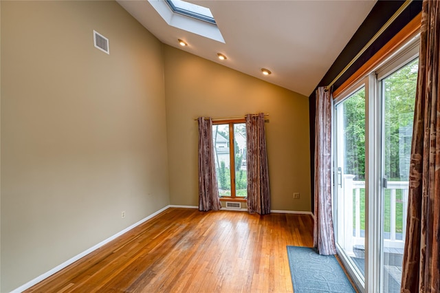empty room featuring a skylight, vaulted ceiling, light wood-style floors, and baseboards