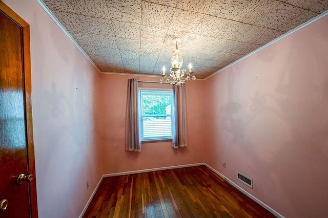 empty room featuring crown molding, a chandelier, hardwood / wood-style floors, and baseboards