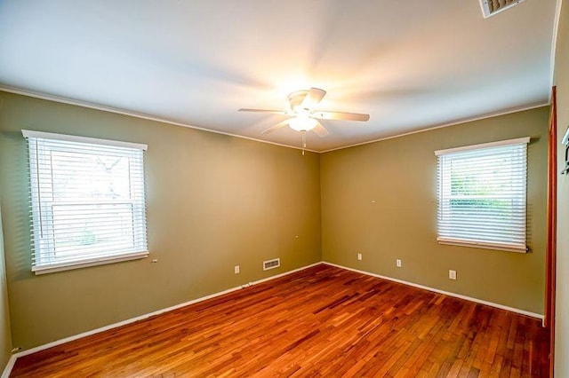 unfurnished room with wood finished floors, a ceiling fan, baseboards, and ornamental molding