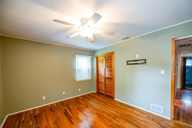unfurnished bedroom with wood finished floors, baseboards, a closet, ornamental molding, and a ceiling fan