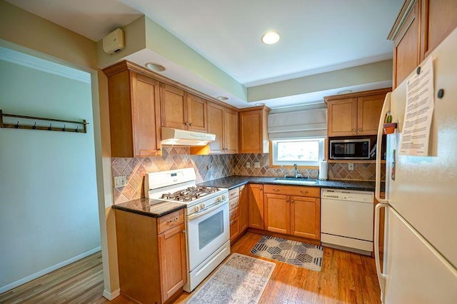kitchen featuring white appliances, under cabinet range hood, a sink, light wood-style floors, and dark countertops