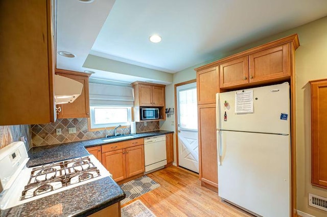 kitchen featuring white appliances, a sink, backsplash, light wood-type flooring, and extractor fan