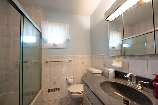 bathroom featuring tile walls, toilet, shower / bath combination with glass door, vanity, and tile patterned flooring